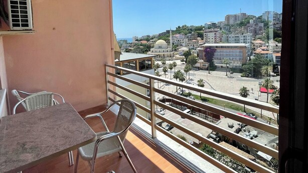 Ein Balkon mit Tisch und Stühlen, mit Blick auf eine Stadtlandschaft aus Gebäuden und Palmen.