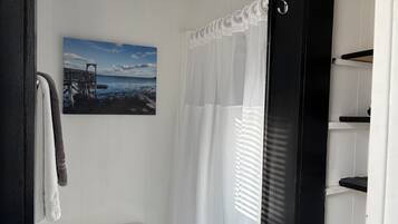 Ein Badezimmer mit Toilette, Handtuchhalter mit Handtüchern, einer weißen Duschvorhang und einem Bild von einem Steg und Wasser an der Wand.