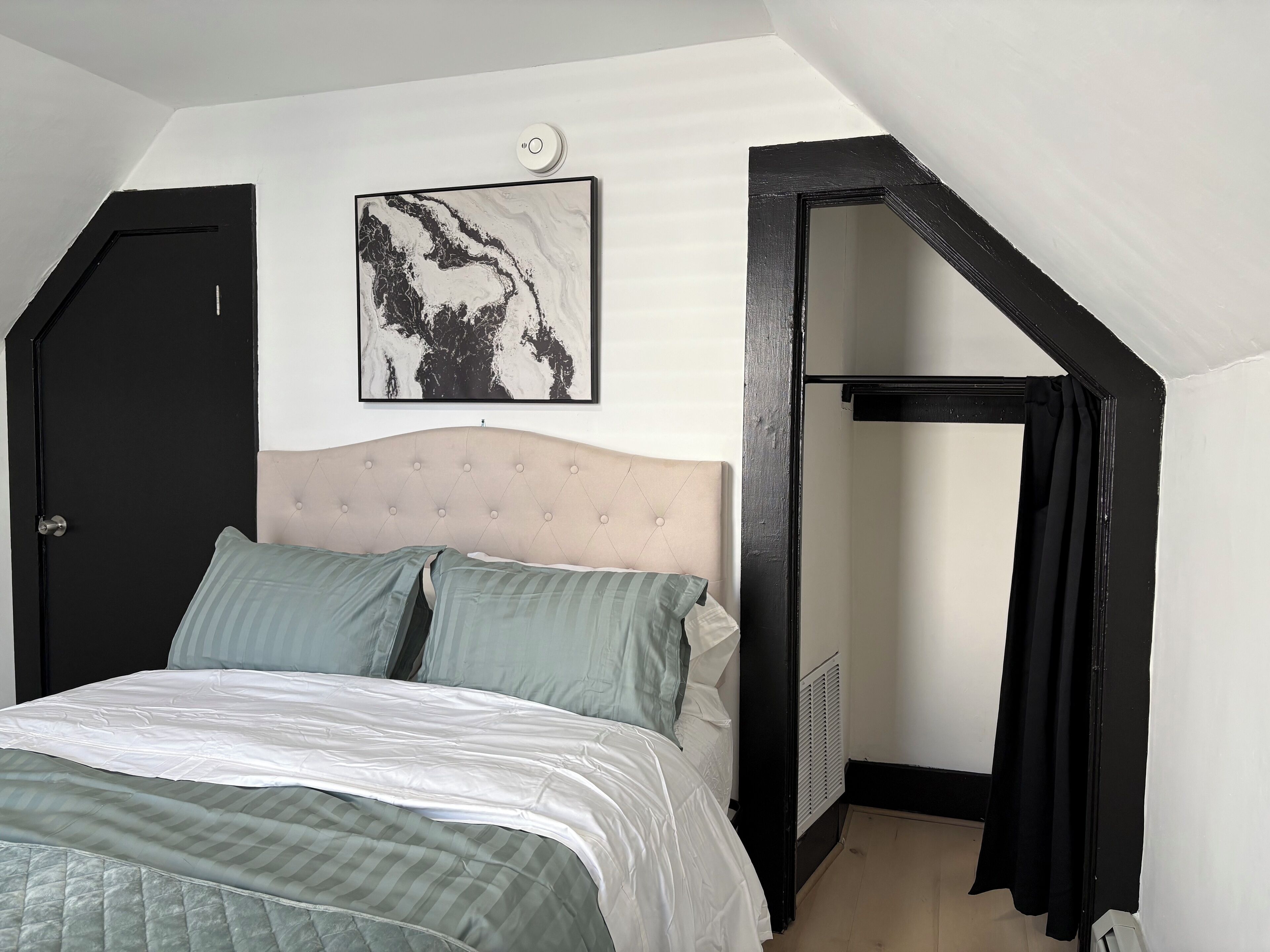 Un dormitorio con cama, cabecera, un cuadro en la pared y una puerta.