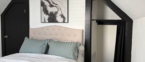 Un dormitorio con cama, cabecera, un cuadro en la pared y una puerta.