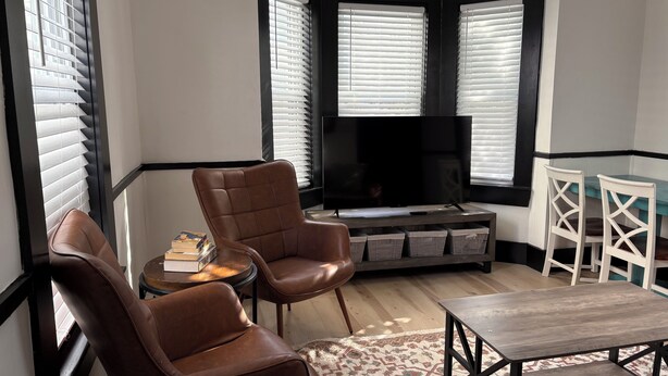 A modern living room with a TV, leather armchairs, a wooden coffee table, and a patterned rug. - 2-Bedroom Home ~ Near Portsmouth/Durham ~ Private Driveway ~ Washer/Dryer (Dover)