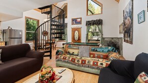 A cozy living room with a spiral staircase, a sofa, a coffee table, and a fireplace. - Mountain Paradise- Family Cabin w Pool Table (Shaver Lake)