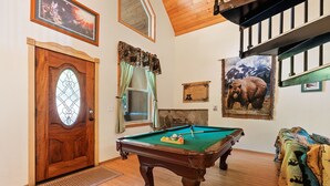 A pool table in a room with a wooden door, a fireplace, and a bear painting on the wall. - Mountain Paradise- Family Cabin w Pool Table (Shaver Lake)