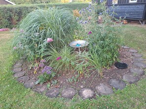 A garden with a variety of plants and a metal birdbath. - Nature, peace and coziness near forest and beach (Nakskov)