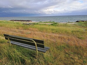 Un banco en un área con césped, con vistas al mar y un cielo nublado.