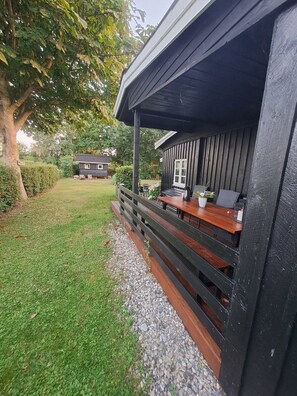 A wooden deck with a table and chairs, surrounded by a gravel path and a grassy area. - Nature, peace and coziness near forest and beach (Nakskov)