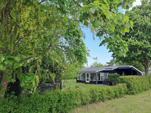 A house with a covered porch, a lawn, and dense greenery. - Nature, peace and coziness near forest and beach (Nakskov)