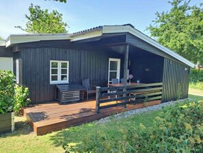 A wooden deck with a table and chairs, a covered patio area, and a small garden area. - Nature, peace and coziness near forest and beach (Nakskov)