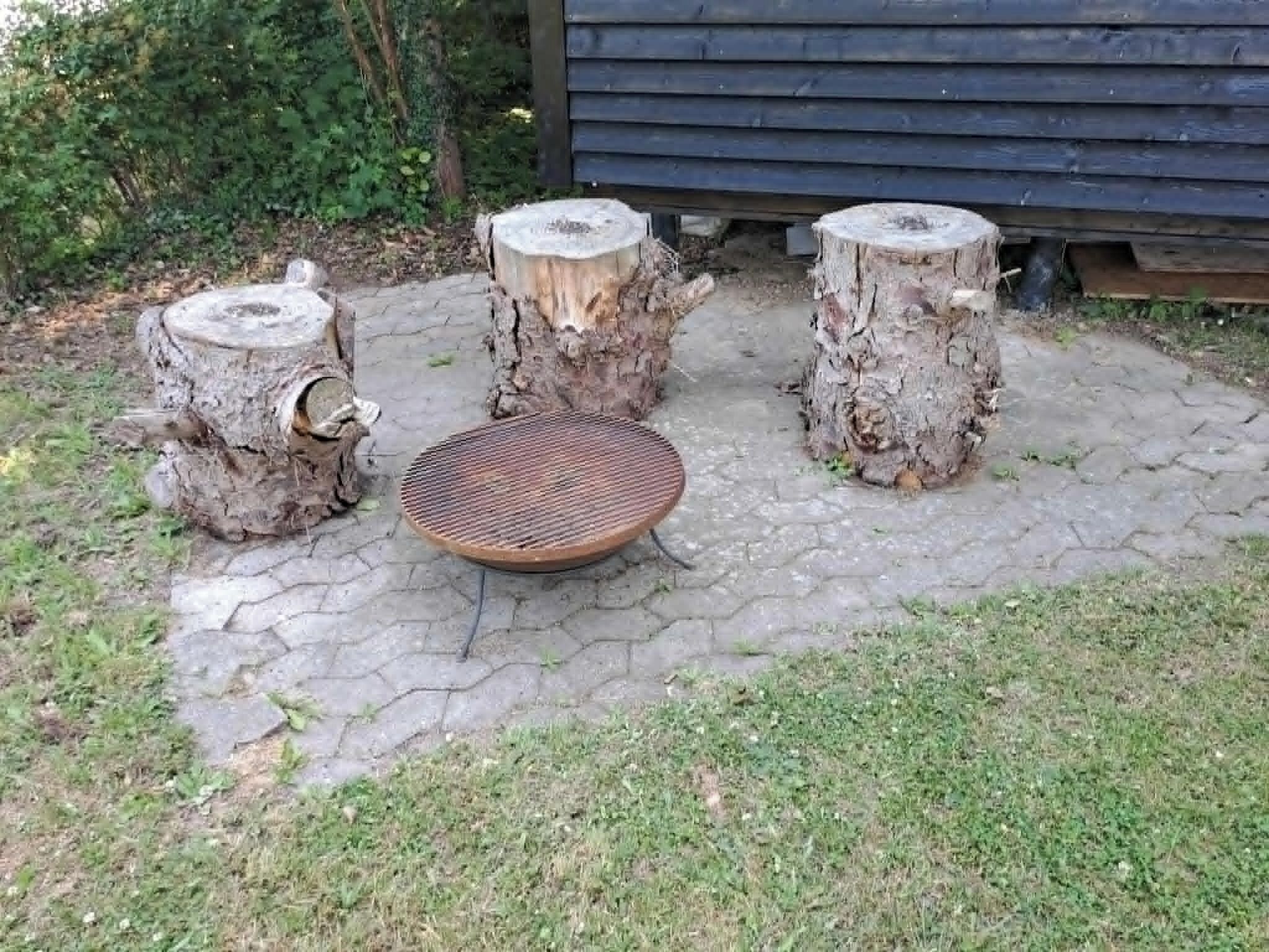 Ein Gartenbereich mit einer runden Sitzgruppe und drei Hockstühlen aus Baumstämmen.