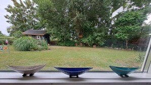 Un rebord de fenêtre orné de trois bols décoratifs, d’où l’on peut admirer une maison et un jardin.