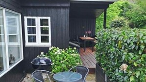 Une terrasse avec une table et des chaises, un barbecue et un petit coin jardin.