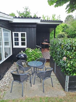 Un patio con una mesa, sillas, una parrilla y un pequeño jardín.
