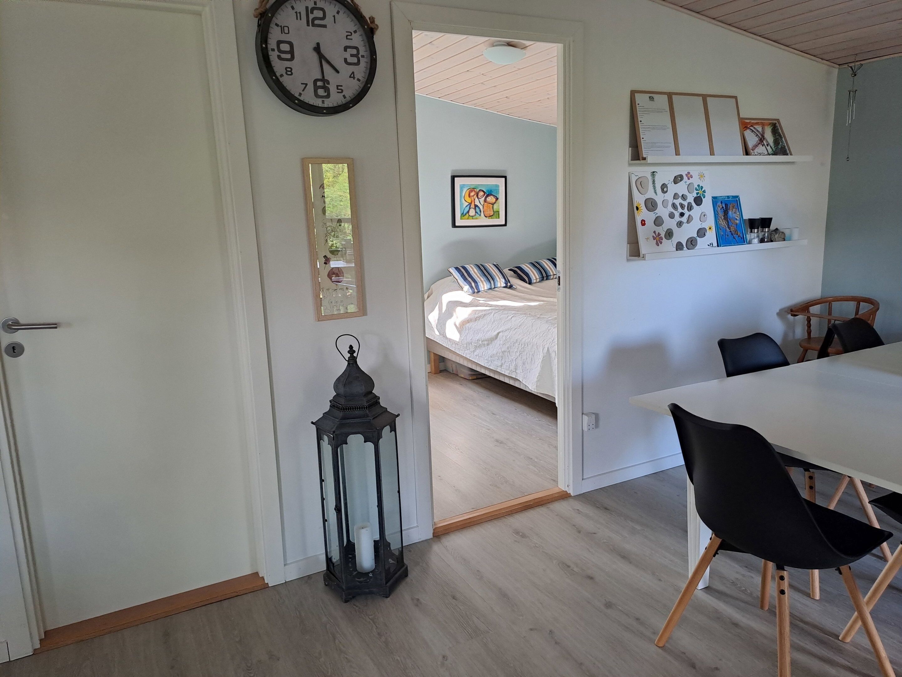 A room with a bed, a dining table with chairs, a wall clock, and a lantern.
