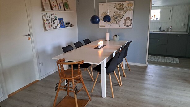 Un espace repas avec une longue table, des chaises, une carte accrochée au mur et une cuisine en arrière-plan.