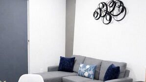 A modern living room with a grey sofa, white chairs, a round table, and a decorative wall piece. - Apartment in Spokane (Spokane)