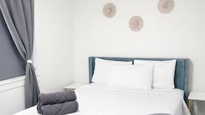 A neatly made bed with a grey blanket and pillows, a dark wooden floor, and a window with grey curtains. - Apartment in Spokane (Spokane)