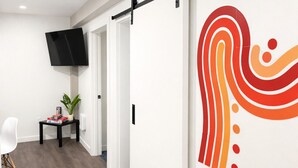 A modern interior with a sliding door, a mounted TV, a small table with a plant, and a wall with a colorful abstract design. - Apartment in Spokane (Spokane)