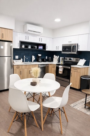 Une cuisine moderne avec des meubles blancs, un réfrigérateur en acier inoxydable, un four à micro-ondes et un coin repas avec des chaises blanches et une table ronde.