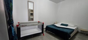Een kamer met een babybedje, een bed, een spiegel en een klein rond tafeltje.