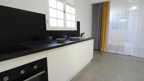 A modern kitchen with a black countertop, white cabinets, and a window with white curtains. - La Fleur Doré studio - Vauclin (Le Vauclin)