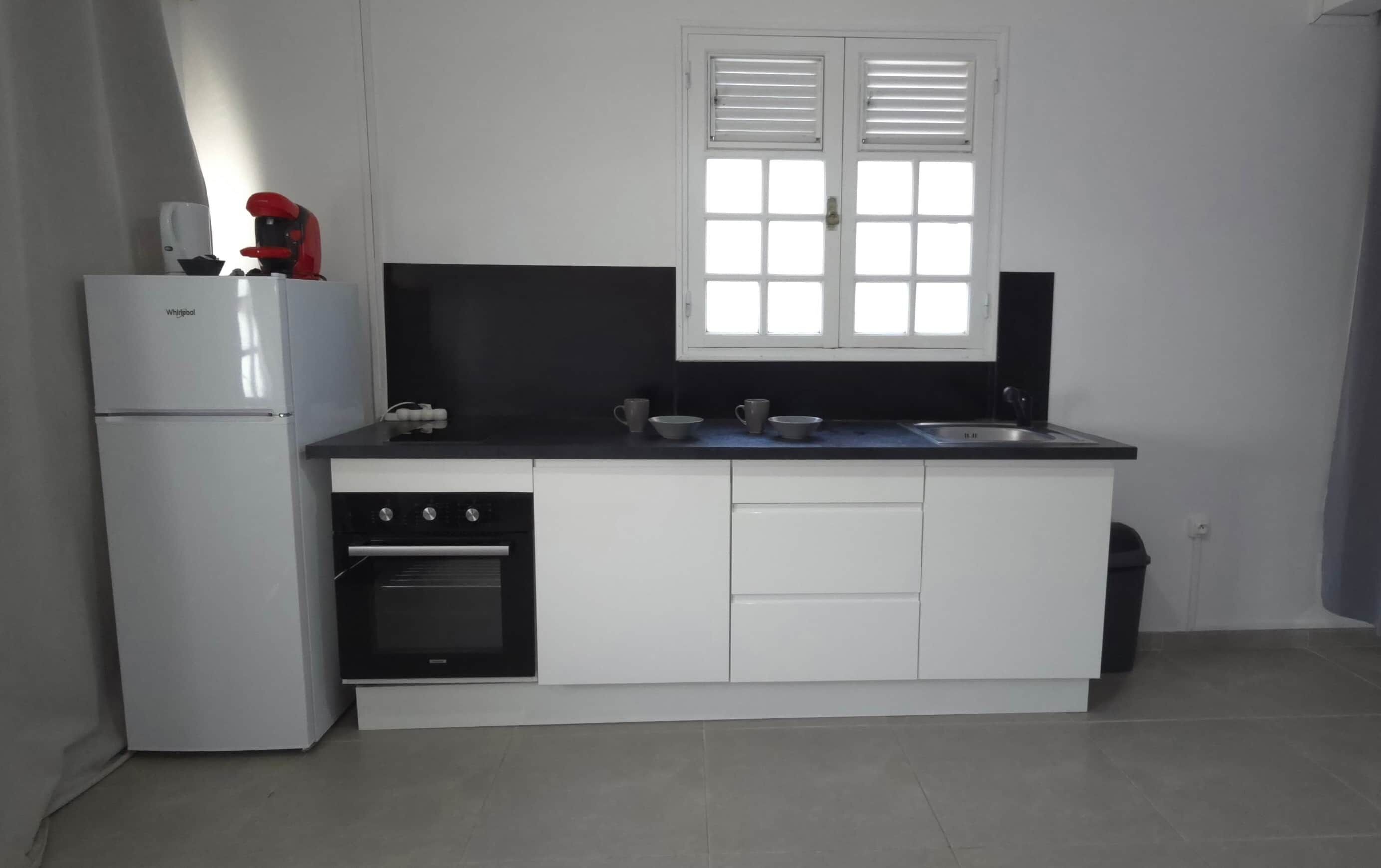 Eine kleine Küche mit Kühlschrank, Backofen und einem Fenster über der Spüle.