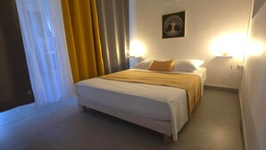 A hotel room with a bed, a nightstand, a wall-mounted lamp, and a door with curtains. - La Fleur Doré studio - Vauclin (Le Vauclin)