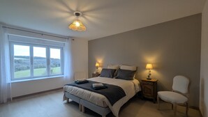 A bedroom with a large bed, two bedside tables with lamps, a chair, and a window with a view of the countryside.