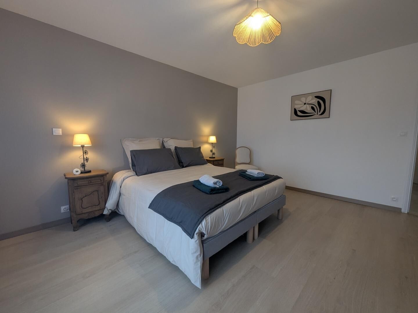 A bedroom with a bed, two bedside tables, a wall-mounted lamp, and a framed artwork.