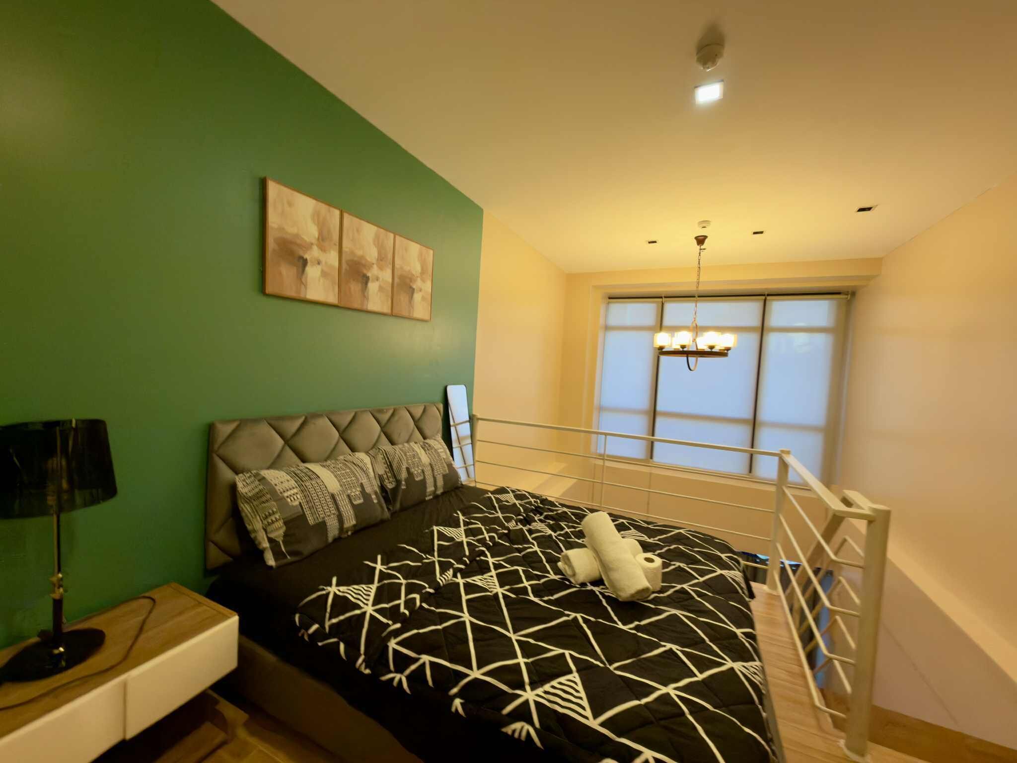 A bedroom with a bed, a nightstand, a lamp, a window with a view, and a ceiling light.