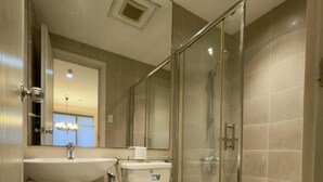A modern bathroom with a glass-enclosed shower, a pedestal sink, and a toilet. - Makati City Gramercy Residences (Makati)
