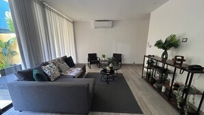 Un salon moderne avec un canapé gris, deux fauteuils noirs, une table basse et une plante posée sur une console en bois.