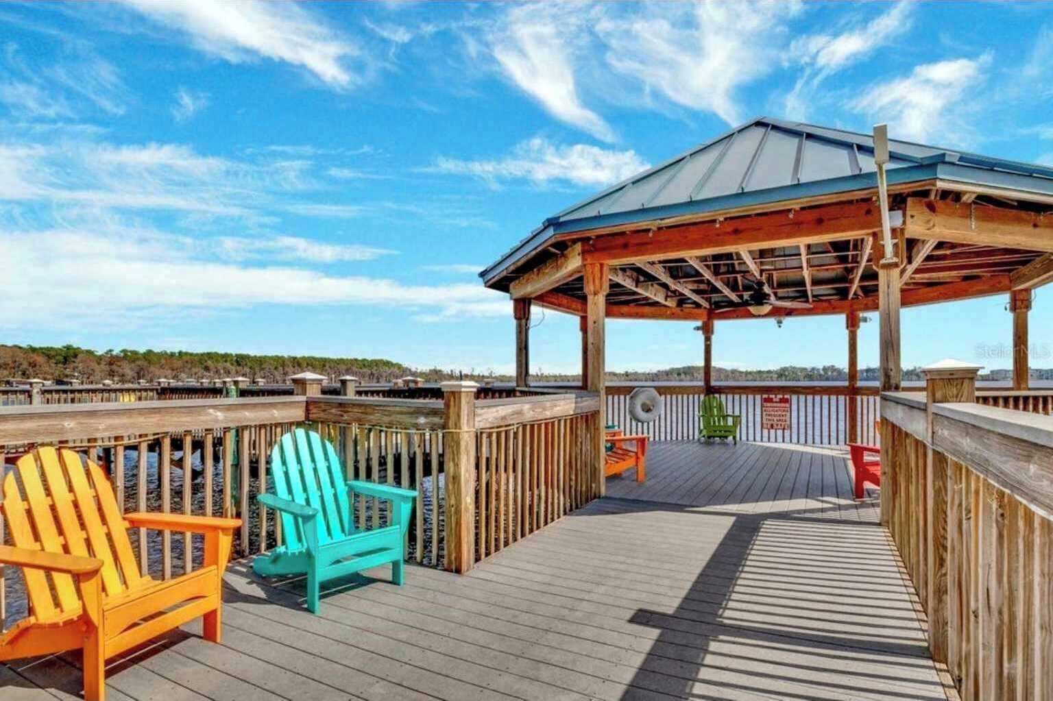 Um deck de madeira com um gazebo, duas cadeiras Adirondack e vista para a água.