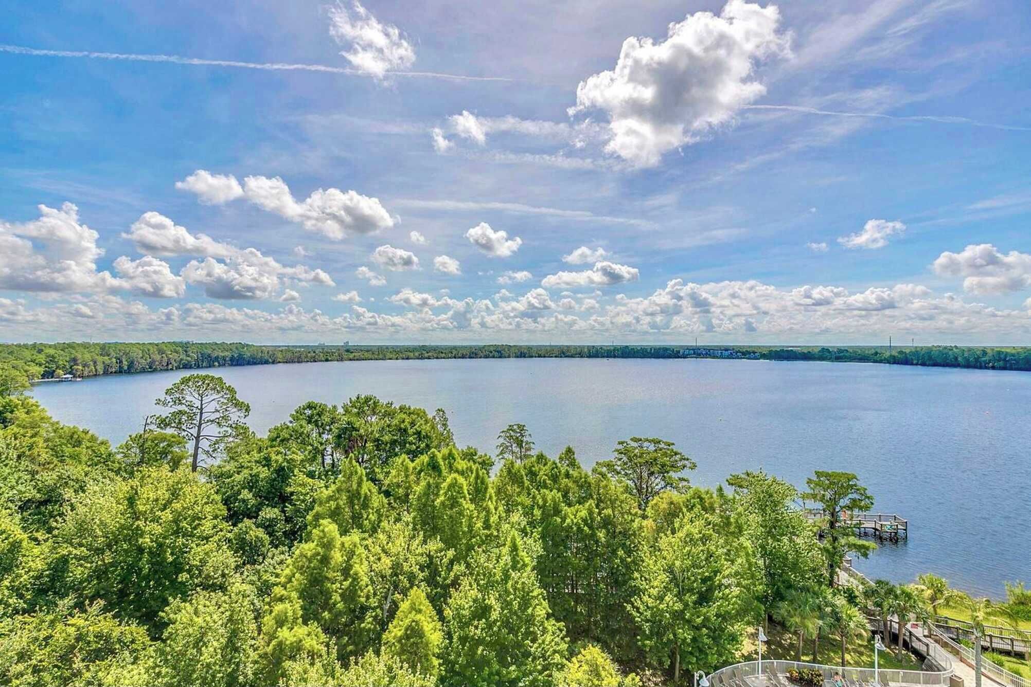 Ein See, umgeben von dichten, grünen Bäumen und einem klaren Himmel mit vereinzelten Wolken.