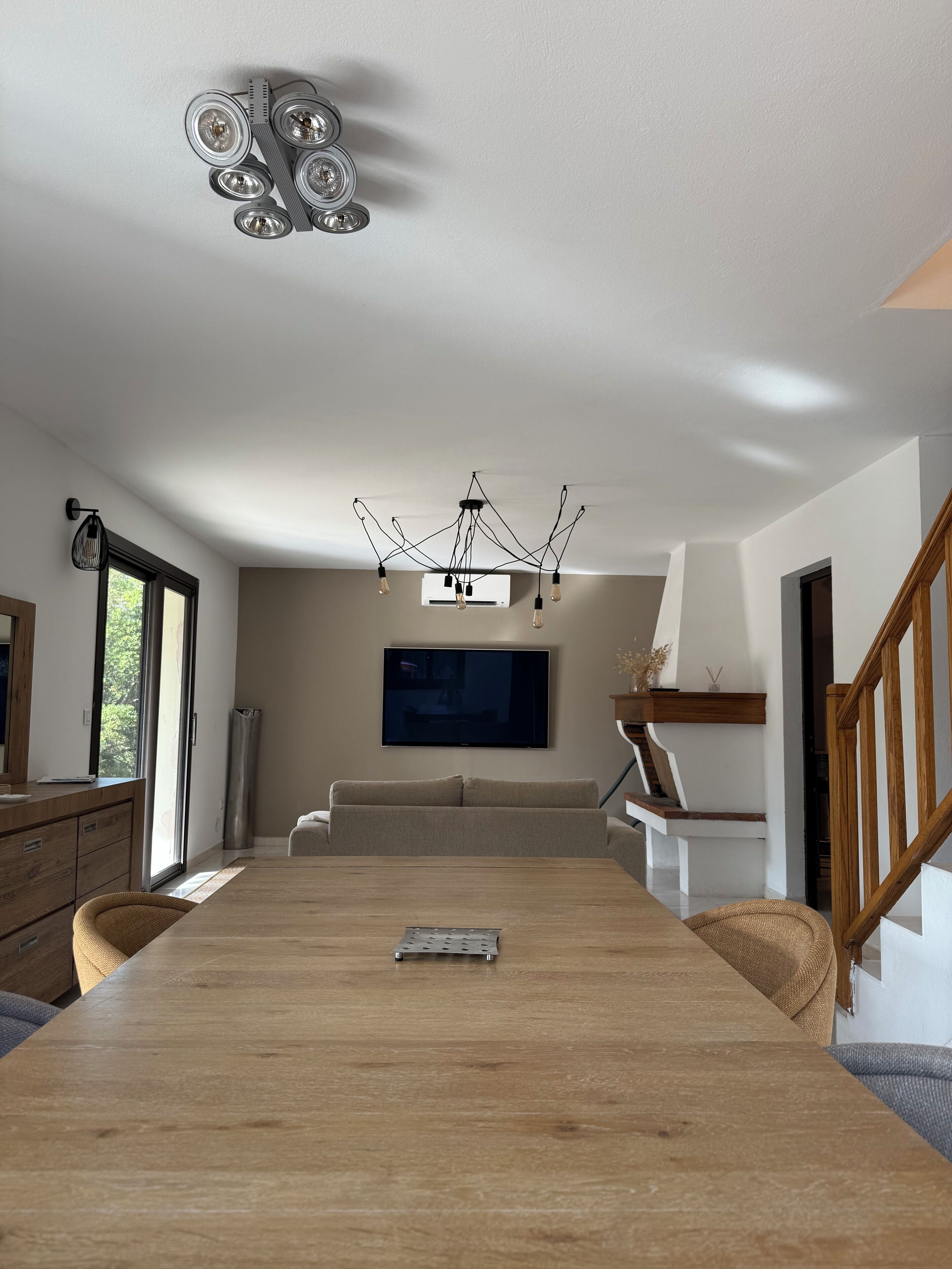 Una sala de estar moderna con una mesa de comedor de madera, un televisor de pantalla plana montado en la pared y una lámpara de techo original.