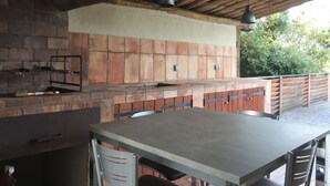 An outdoor kitchen with a brick oven, metal table, and chairs. - 2bedroom house with private heated pool 5mn from the beach (Figari)