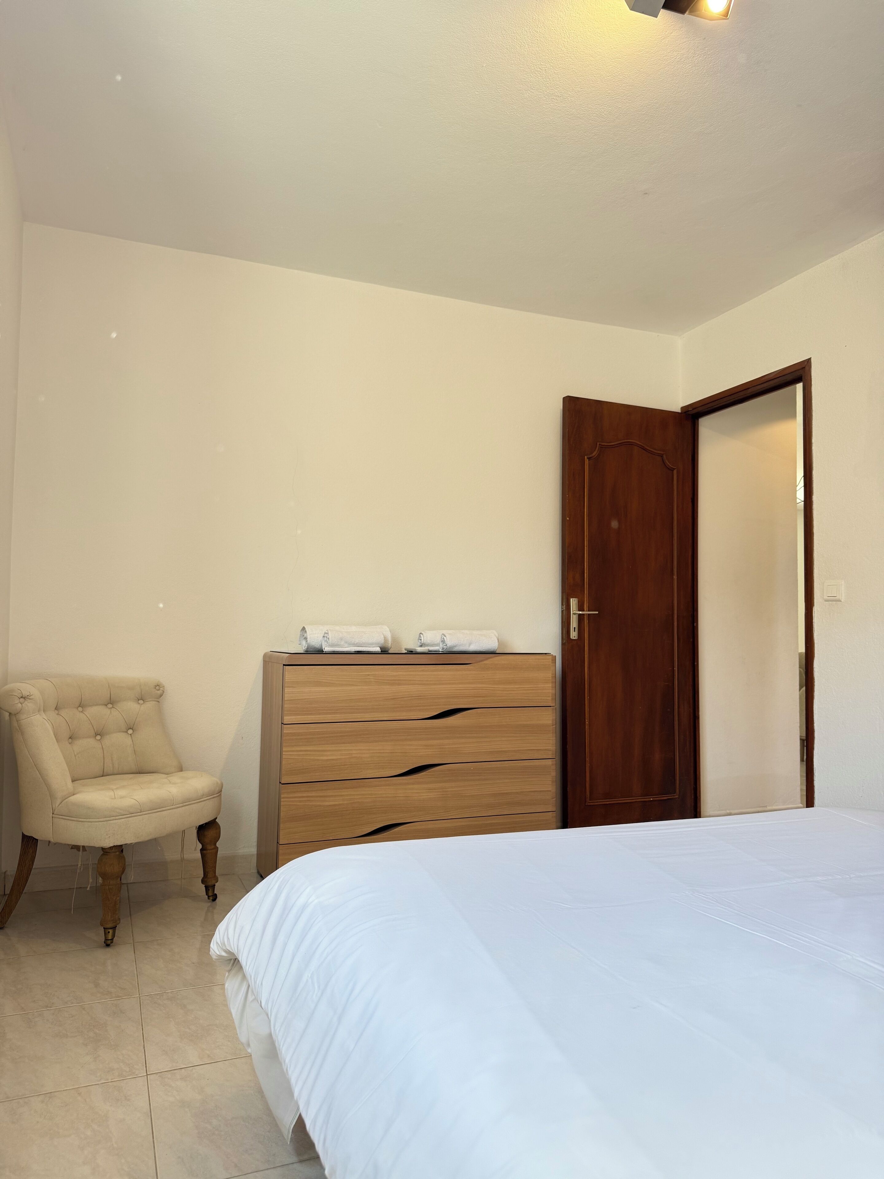 Une chambre à coucher avec un lit, une commode en bois, une chaise et une porte.