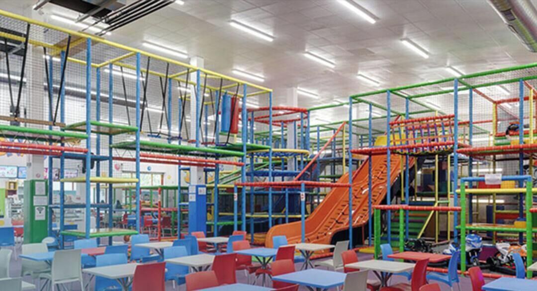 Ein großer Indoor-Spielbereich mit bunten Spielgeräten, Tischen und Stühlen.