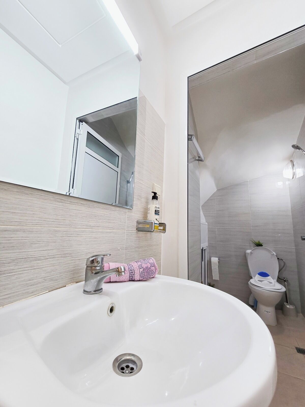 A modern bathroom with a white sink, a mirror, and a toilet.