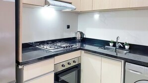 Une cuisine moderne avec des meubles de couleur bois clair, un plan de travail noir, une cuisinière à gaz, un four et un lave-vaisselle.