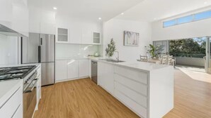 A modern kitchen with white cabinetry, a central island, and a built-in dishwasher. - Luxe Coastal Escape. Walk to beach, cafe and shops. (Crescent Head)