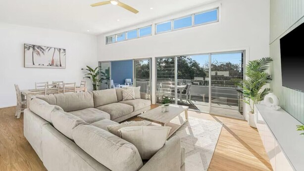 A modern living room with a sectional sofa, a ceiling fan, and large sliding glass doors leading to an outdoor area. - Luxe Coastal Escape. Walk to beach, cafe and shops. (Crescent Head)