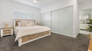 A bedroom with a bed, bedside tables, a wardrobe, and a ceiling fan. - Luxe Coastal Escape. Walk to beach, cafe and shops. (Crescent Head)