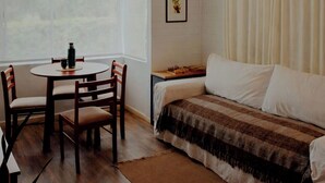 A room with a wooden floor, a round table with chairs, a bed with a striped blanket, a ceiling fan, and a window with curtains. - Exclusive Cabin in La Aventura Complex (Posadas)