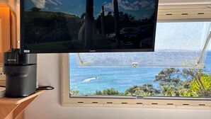 A television mounted on a wall, a window with a view of the sea, and a Nespresso coffee machine. - Goat-Island Beach Front Get-Away! (Leigh)