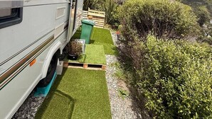 A white RV parked on a gravel driveway with a green artificial lawn leading to a wooden gate. - Goat-Island Beach Front Get-Away! (Leigh)