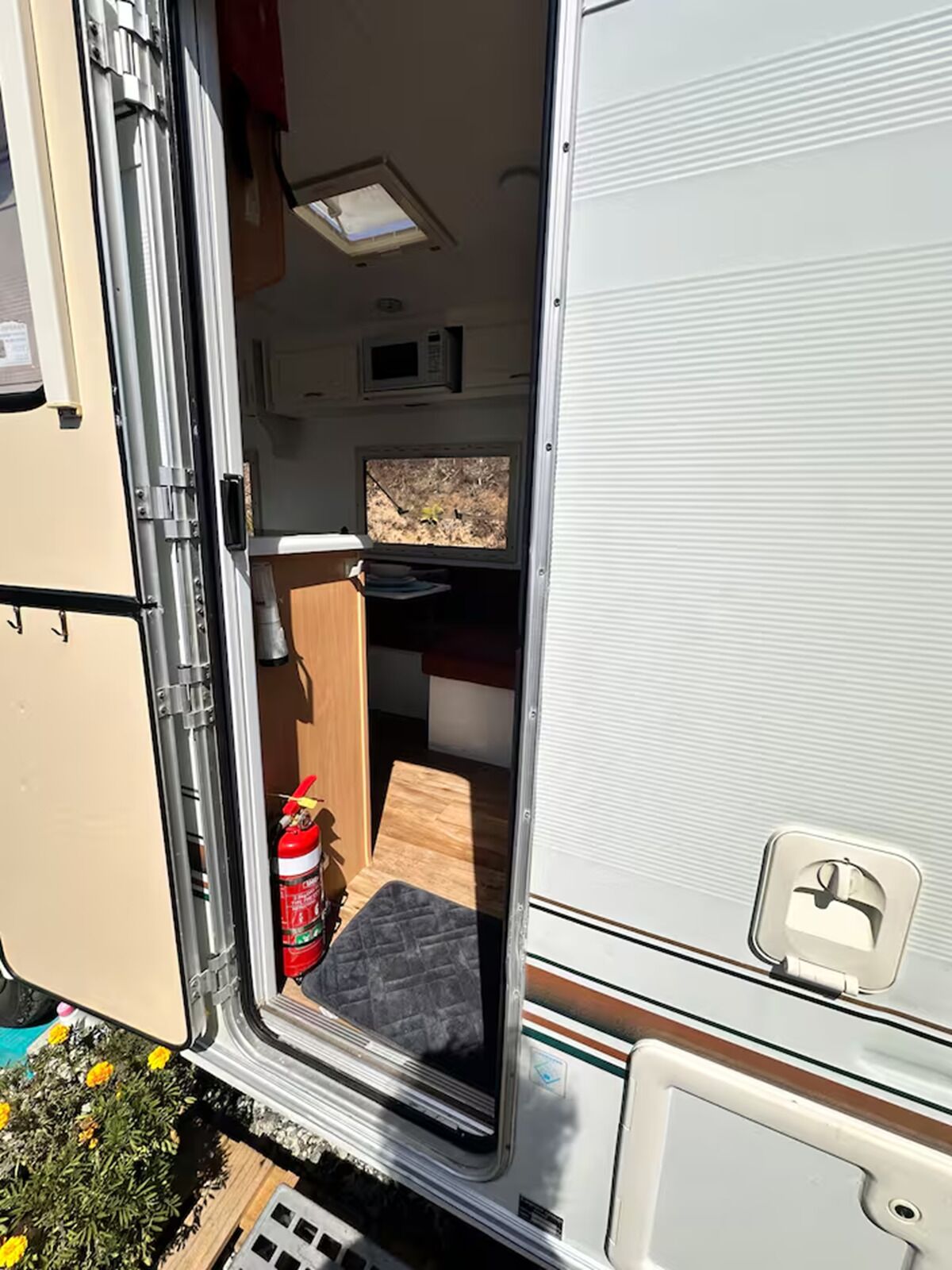 An RV interior with a kitchenette, a small window, and a fire extinguisher.