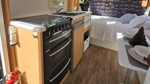 A compact RV kitchen with a stove, oven, and sink, a small dining area with a table and chairs, and a bed with a blue animal print headboard. - Goat-Island Beach Front Get-Away! (Leigh)