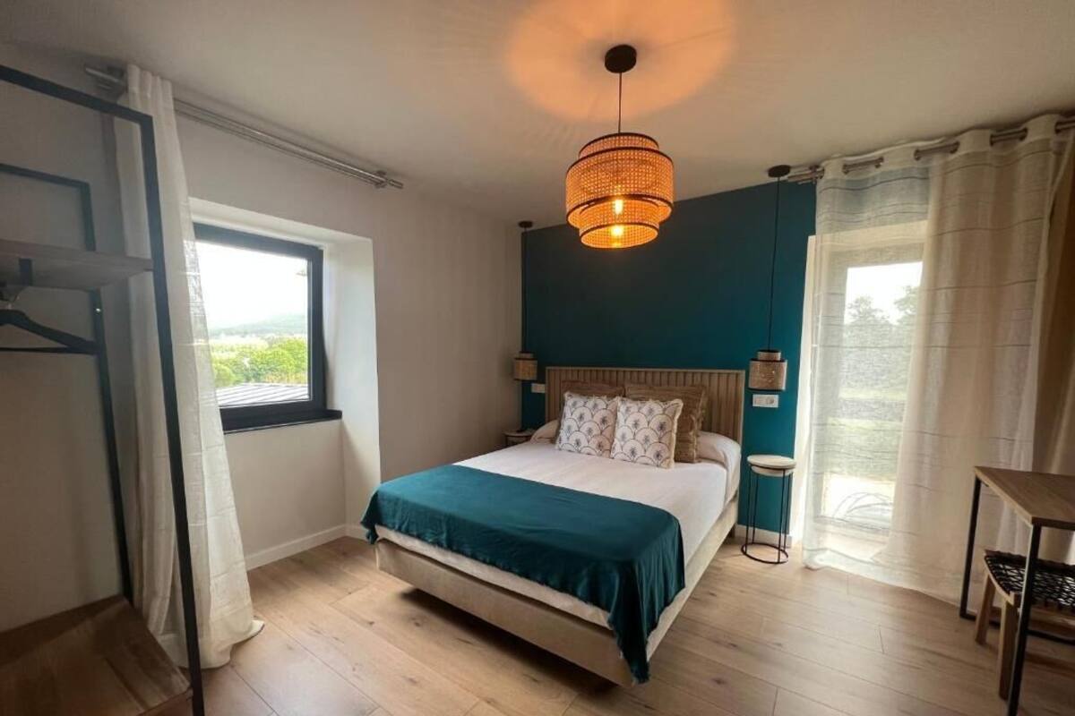 Ein Schlafzimmer mit einem Bett, einer Pendelleuchte, einem Fenster und Blick ins Freie.
