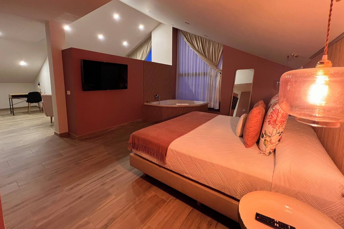 Ein modernes Schlafzimmer mit einem großen Bett, einem integrierten Fernseher, einem Schminktisch mit Spiegel und einer Deckenleuchte.