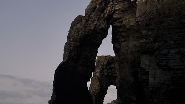 A natural rock formation arching over a beach.